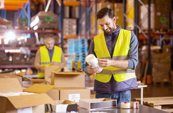 Storehouse worker. Nice bearded man putting labels on products while working in the storehouse